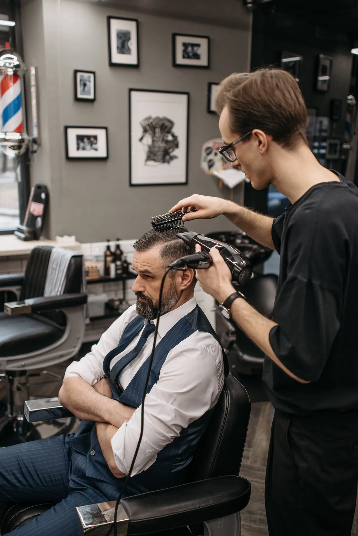 Friseur föhnt einem Kunden im Anzug die Haare in Form